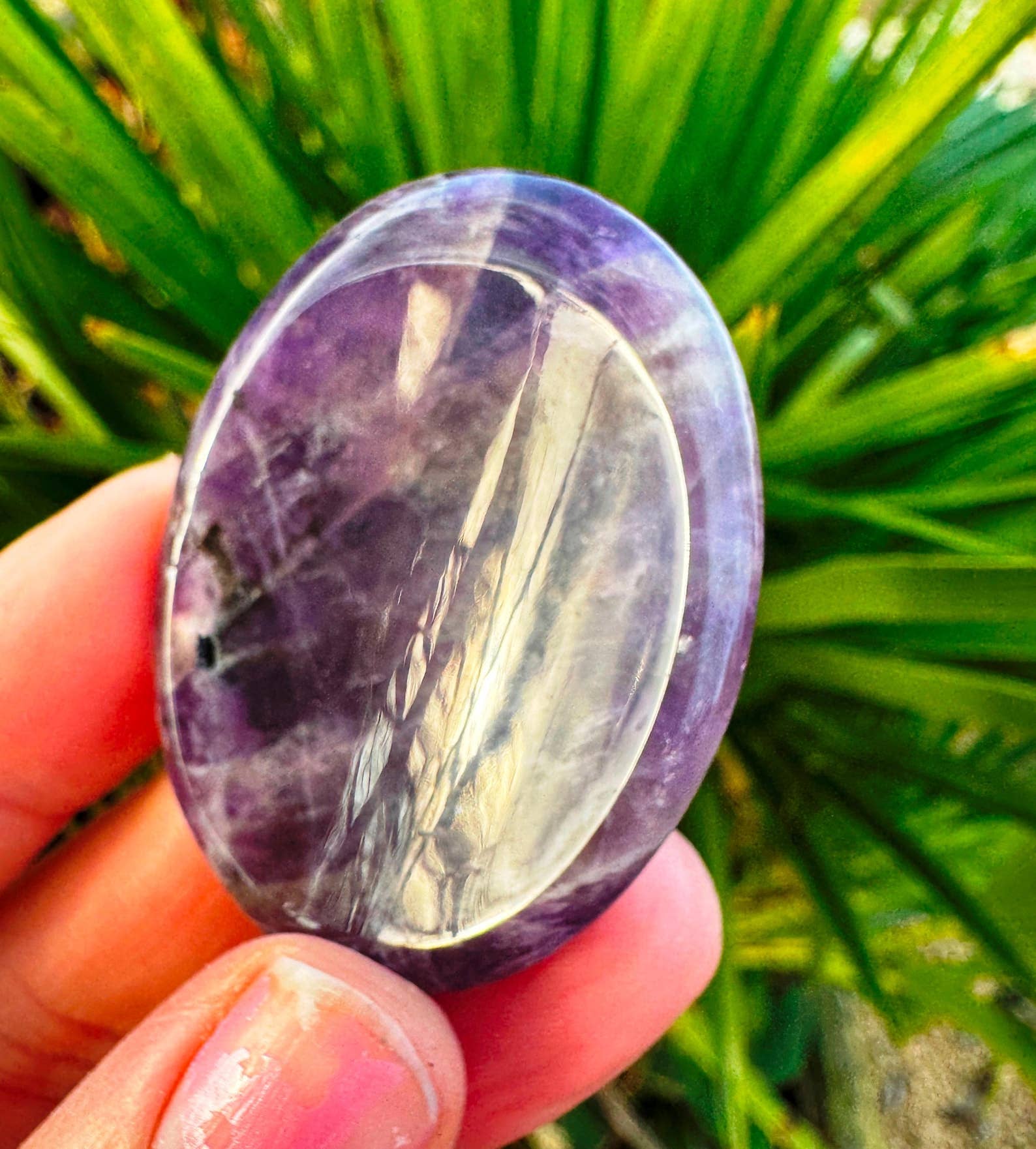 Oval-shaped purple stone held in a hand with a green leafy background