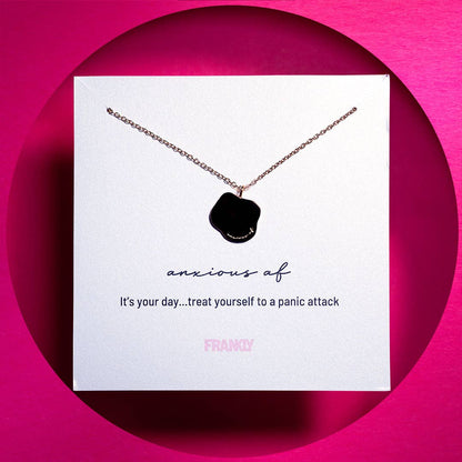 anxious af text engraving on a pendant with gold chain on a white card on a pink background