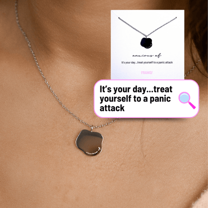 Necklace with a pendant worn on a person's neck, with a humorous card in the background.