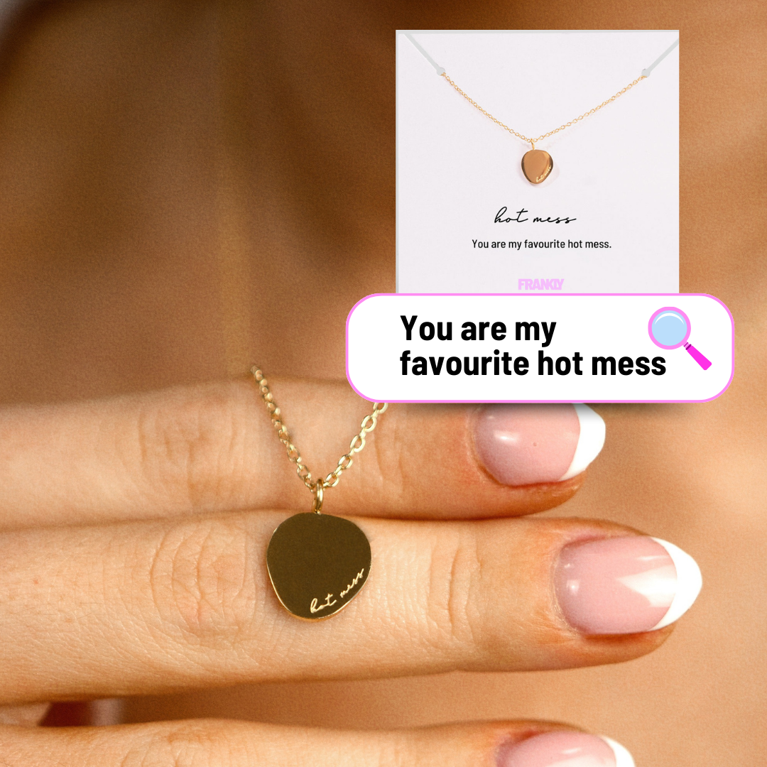 Gold necklace with heart pendant on a hand, card in the background with text.