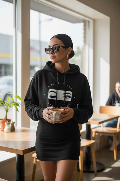 Woman wearing a black hoodie with a logo, holding a cup, in a casual setting.