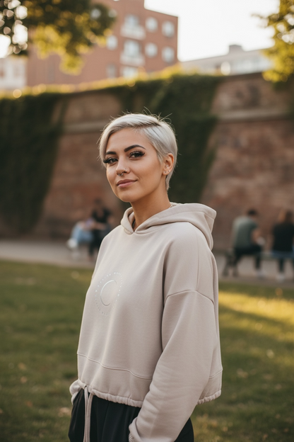 Woman wearing a beige hoodie standing outdoors with a blurred background