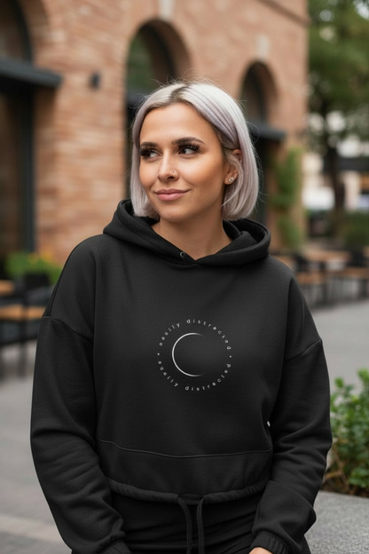 Woman wearing a black hoodie with a logo, standing outdoors.