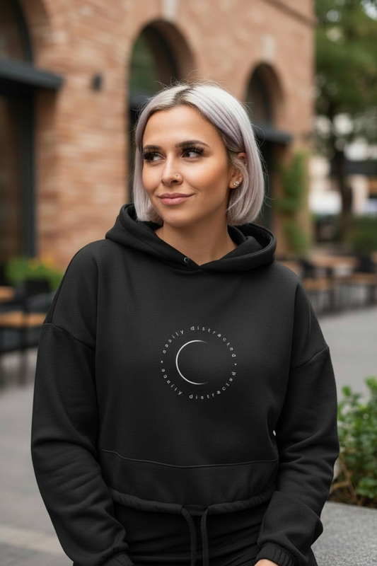 Woman wearing a black hoodie with a logo, standing outdoors.