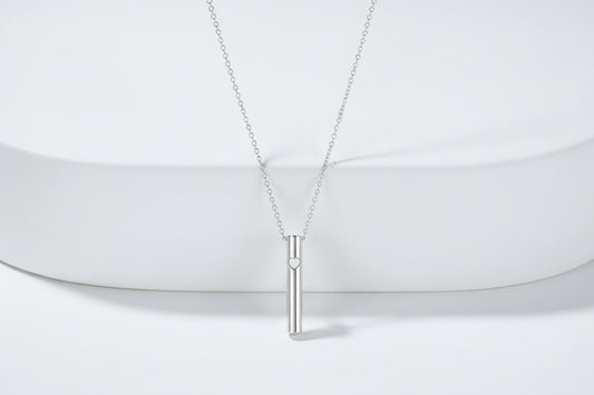 Silver necklace with a cylindrical pendant on a light gray background