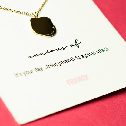 Necklace with a gold pendant on a card with humorous text, against a pink background