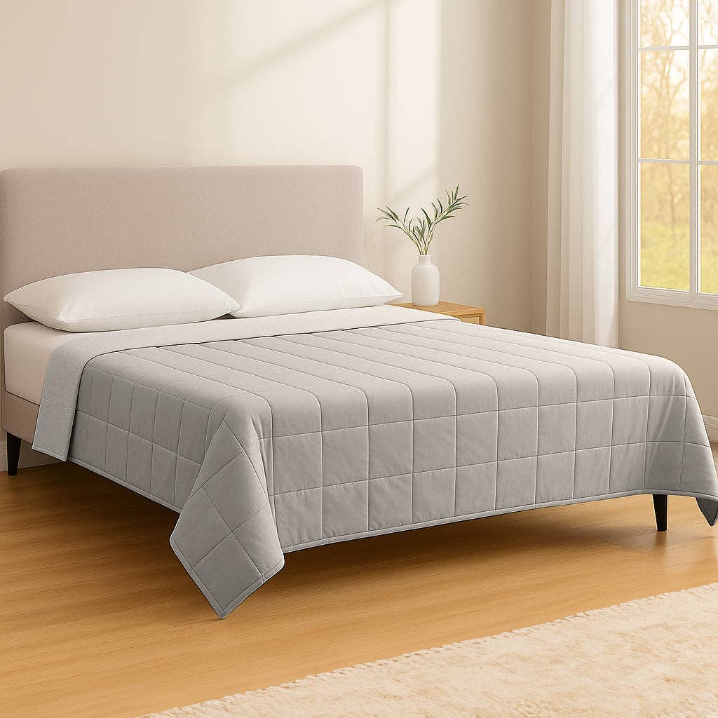 Gray quilted cover on a bed in a bright bedroom with wooden floor and window.